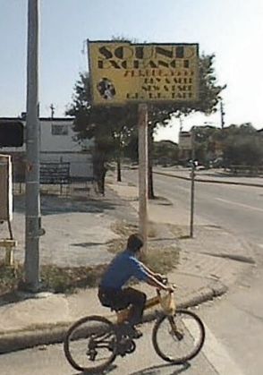 Sound Exchange Record Store in Houston with a young man in a blue shirt bicycling in the parking lot.